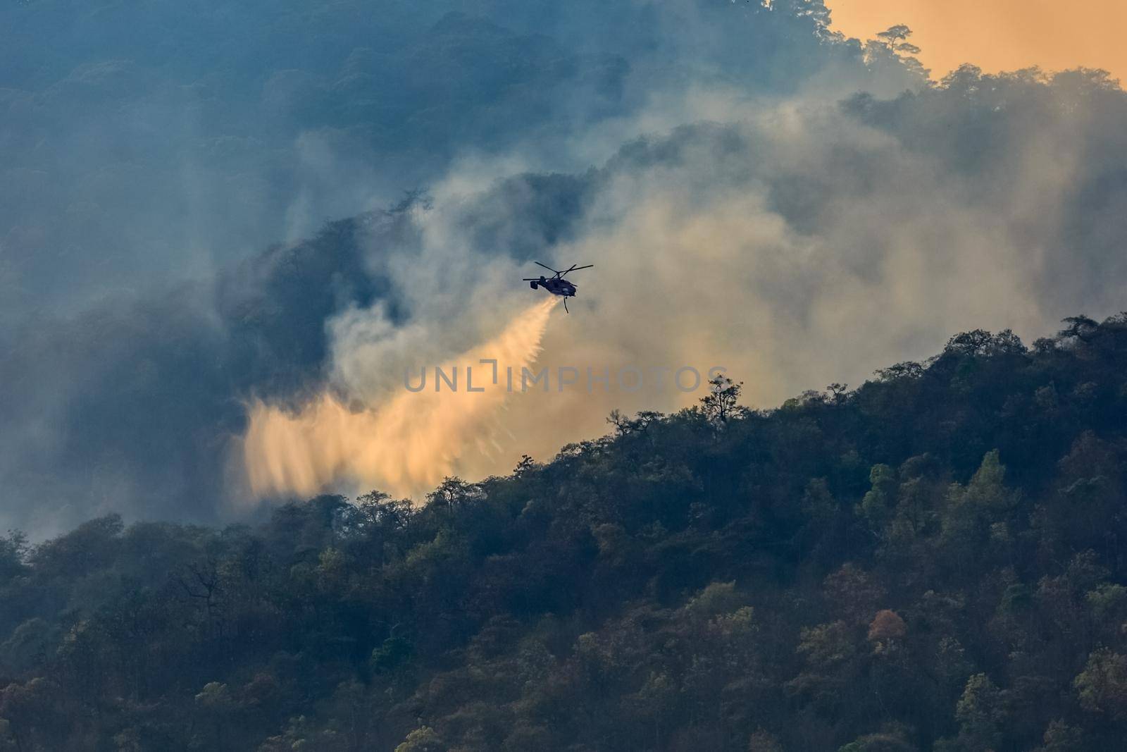 Firefighting helicopter dropping water on forest fire