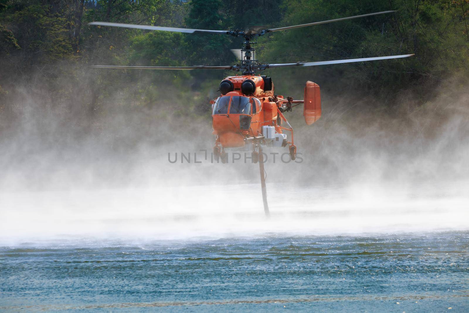 Firefighting helicopter is hovering over the pond to refills water