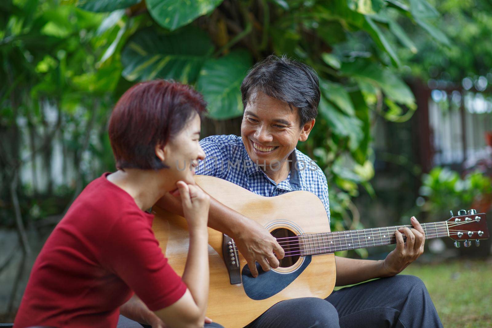 Middle aged  couple playing guitar while relax sitting on bench in backyard. by toa55