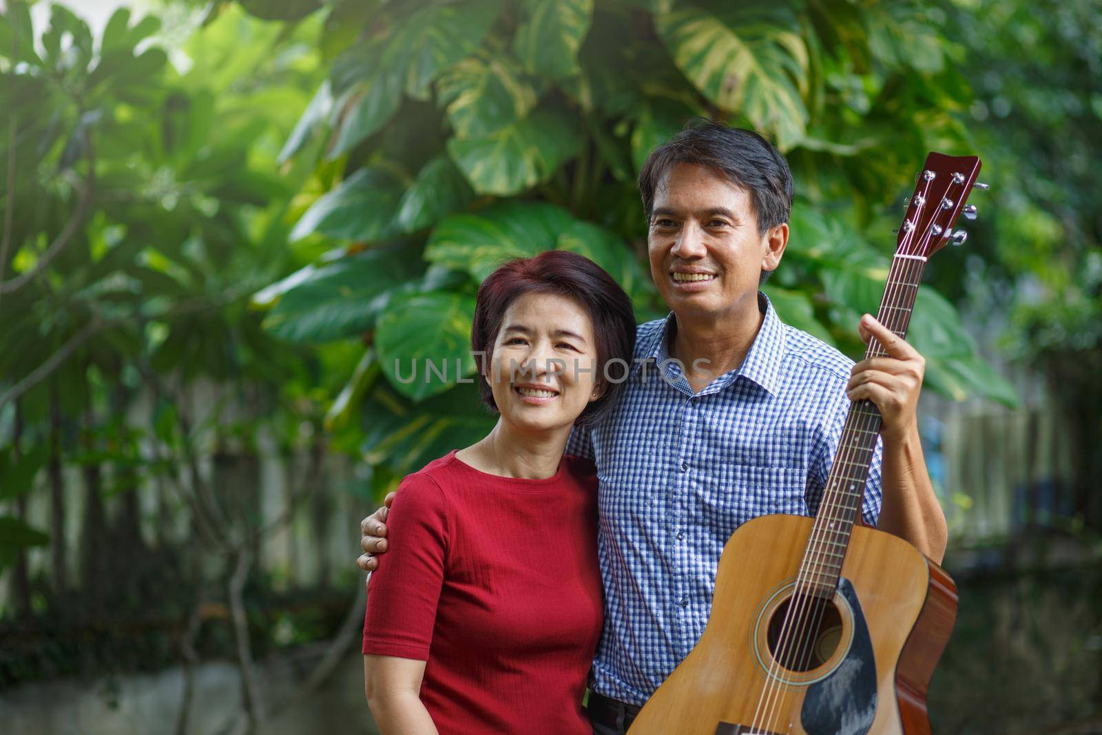 Middle aged  couple playing guitar while relax sitting on bench in backyard.