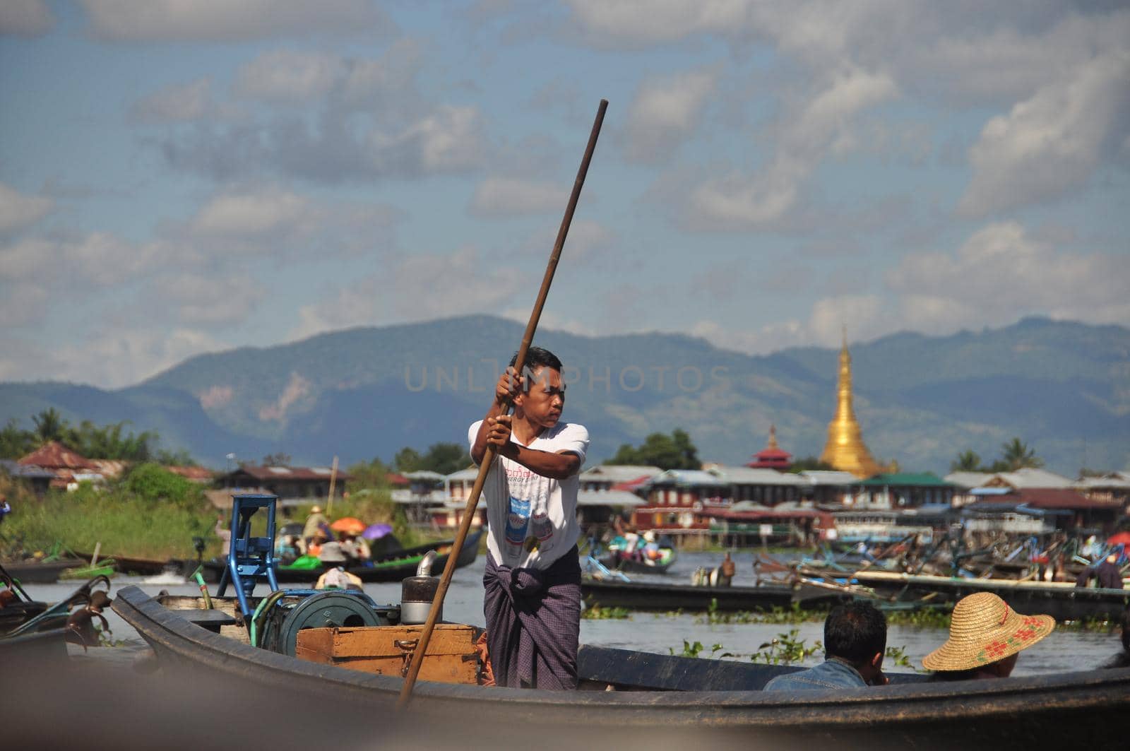 INLE LAKE, MYANMAR - 28 NOVEMBER 2016 View of ethnic man sailing boat pushing with long wooden pole from bottom on Inle lake in sunlight, Myanmar. Man sailing boat with pole