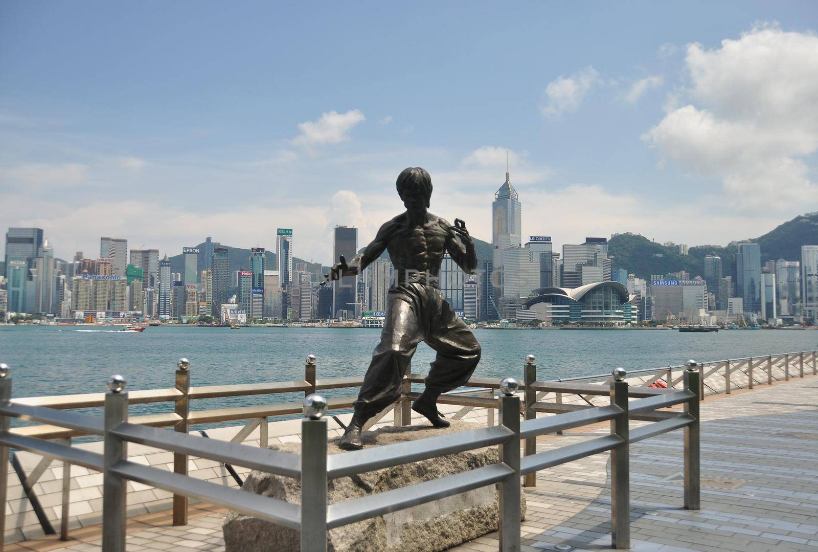 HONG KONG - 23th FEBRUARY, 2015 Metal fighter statue on pier of city coastline with highrise buildings on background, Hong Kong. Statue of Bruse Lee fighter on seashore of city.