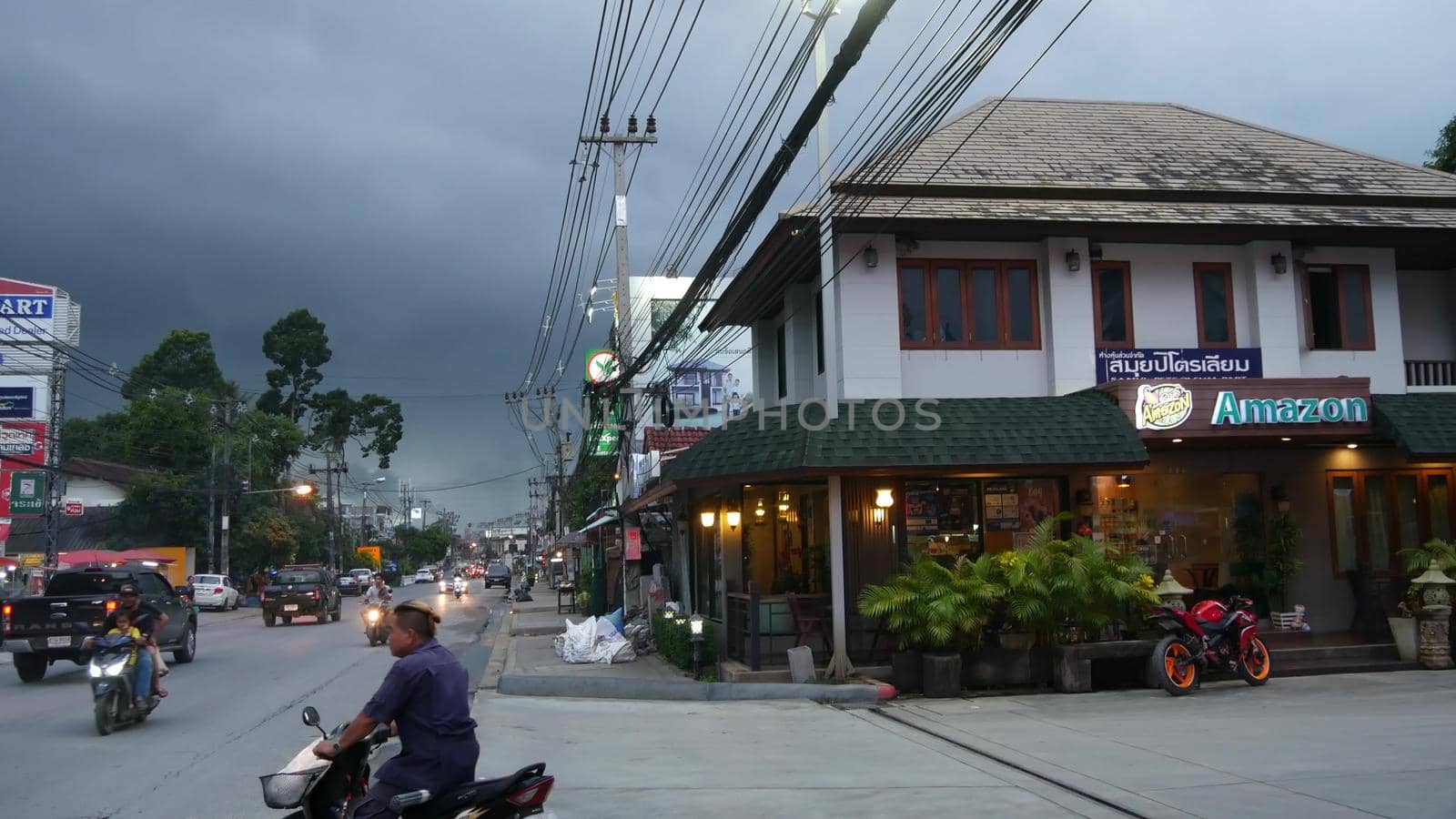 KOH SAMUI ISLAND, THAILAND - 21 JUNE 2019 Busy transport populated city street in cloudy day. Typical street full of motorcycles and cars. Thick blue clouds before storm during wet season