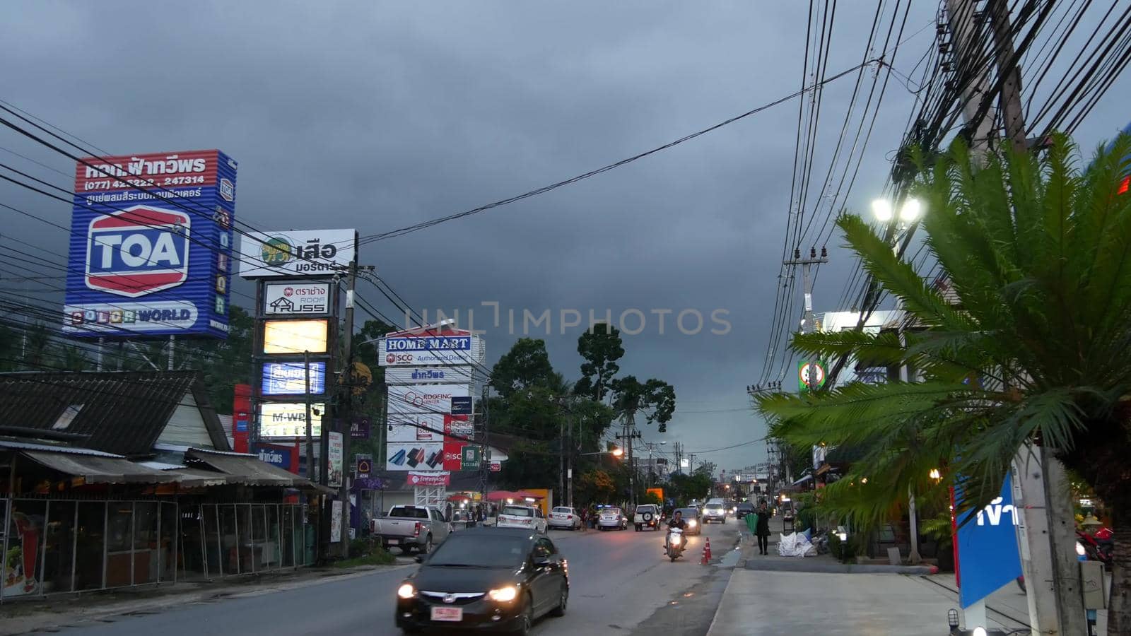 KOH SAMUI ISLAND, THAILAND - 21 JUNE 2019 Busy transport populated city street in cloudy day. Typical street full of motorcycles and cars. Thick blue clouds before storm during wet season. by DogoraSun