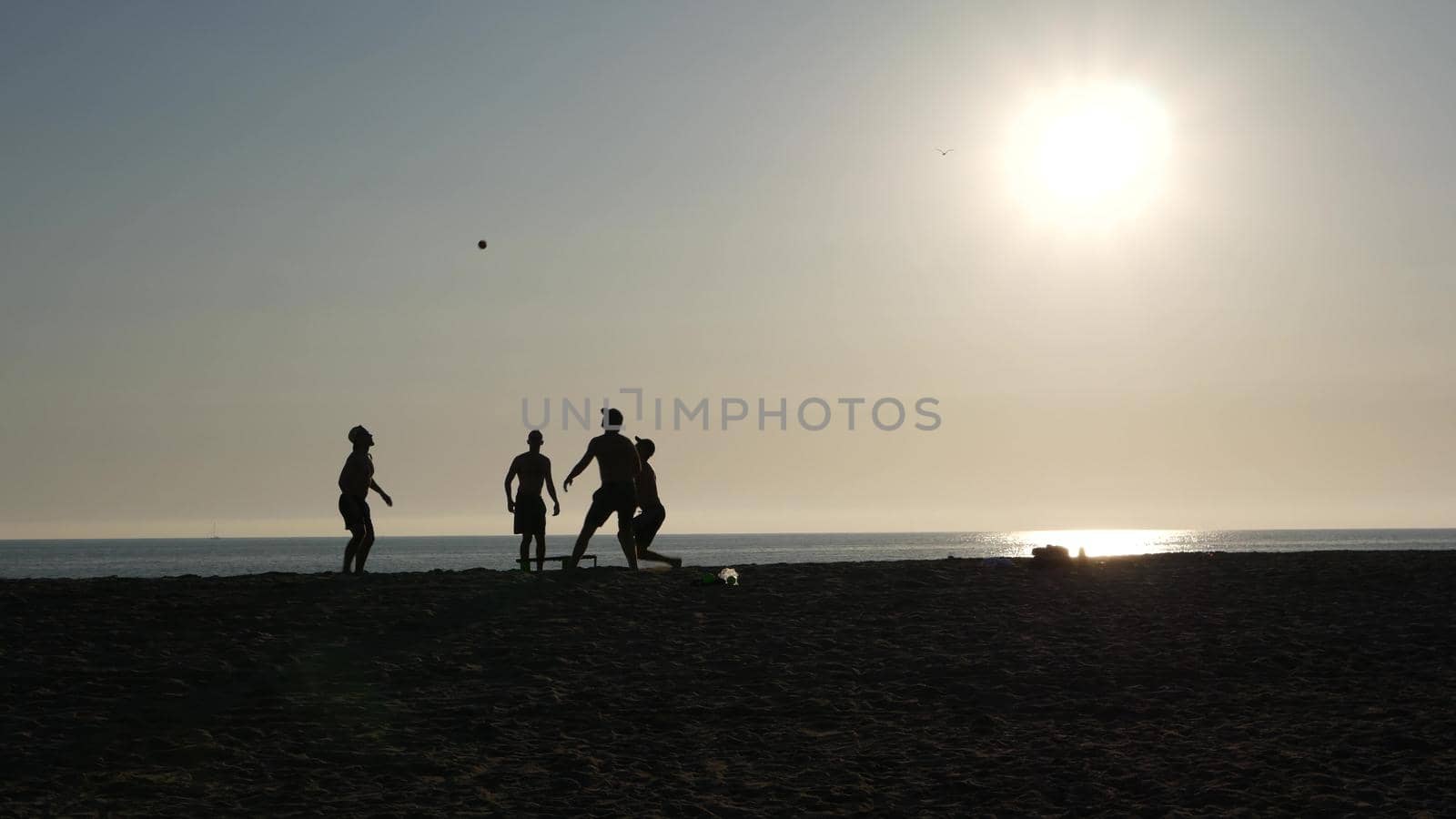 NEWPORT, LOS ANGELES CA USA - 3 NOV 2019: California summertime beach, young men playing roundnet or spike ball game with trampoline and having fun near pacific ocean. Silhouette against sunshine.