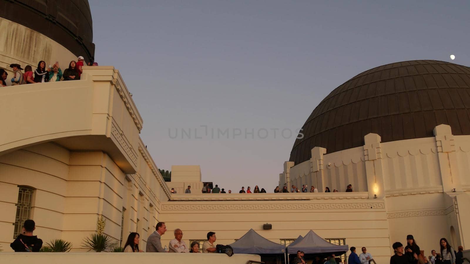 LOS ANGELES, CALIFORNIA, USA - 7 NOV 2019: Griffith observatory viewpoint. Crowd on vista point, people watching sunset over city and Hollywood sign. Many multiracial tourists look at golden sundown by DogoraSun