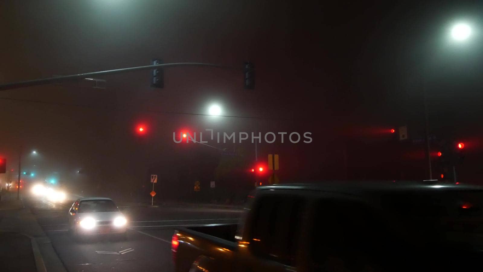 VISTA, CALIFORNIA USA - 24 JAN 2020: Marine layer, dense fog on driveway crossroad at night. June gloom, misty nebulous bad weather. Dangerous low visibility on road intersection. Car traffic safety by DogoraSun