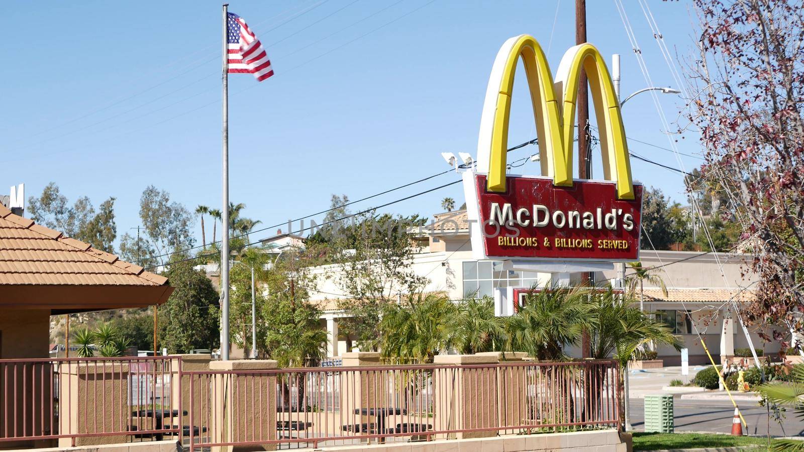 VISTA, CALIFORNIA USA - 16 FEB 2020: McDonalds logo sign and American flag. Yellow letter M icon and Stars and Stripes. Golden Arches emblem, brand sign in suburban district. Food restaurant on street