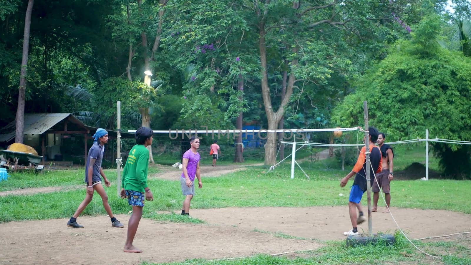 ANG THONG, THAILAND - 9 JUNE 2019: Thai teenagers playing sepak takraw in park. Group of men playing kick volleyball against green trees in yard in local settlement. Traditional national sport game.
