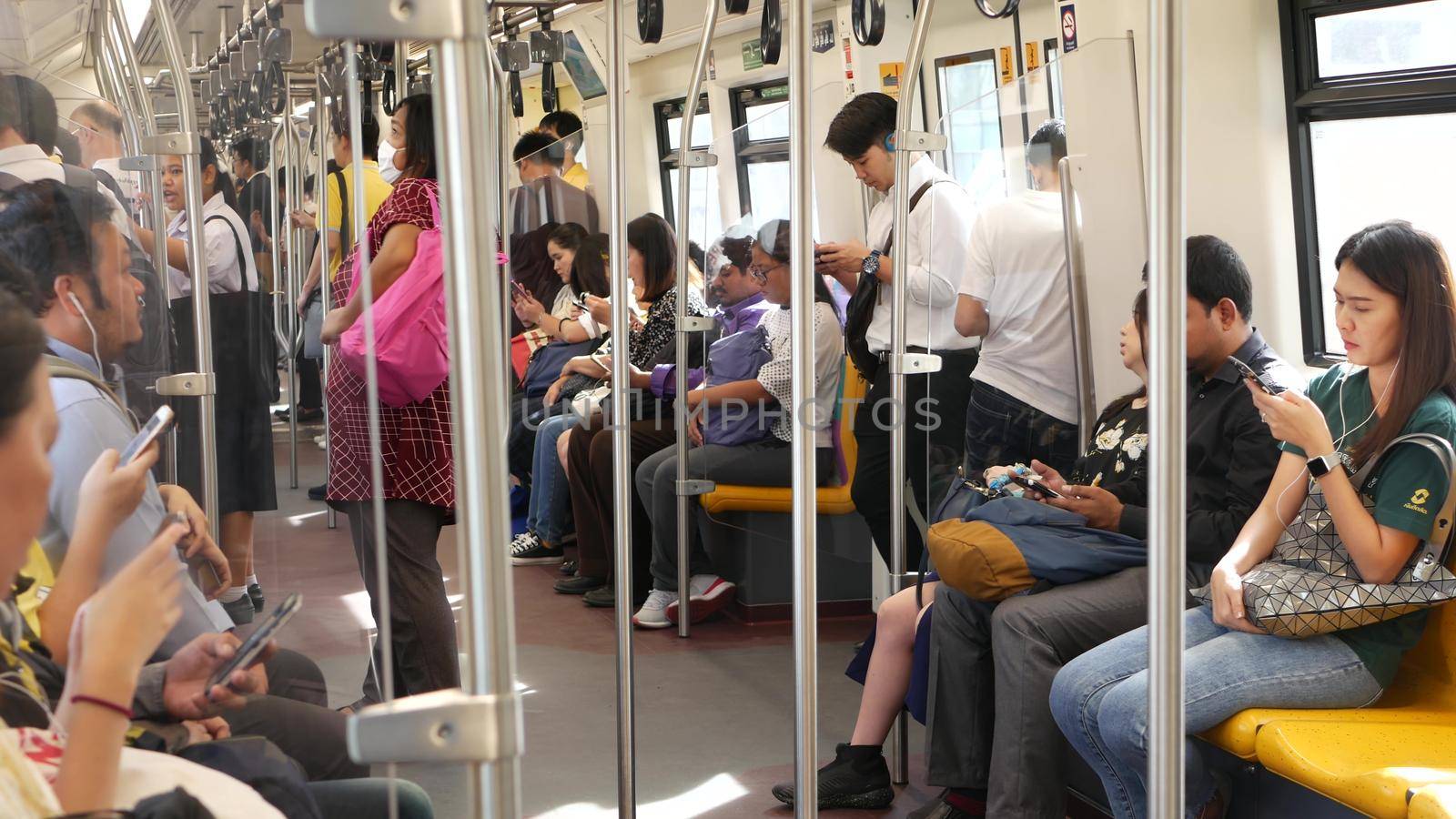 BANGKOK, THAILAND - 10 JULY, 2019: Asian passengers in train using smartphones. Thai people online surfing internet in bts car. Public transportation. Addiction from social media and phone in subway. by DogoraSun