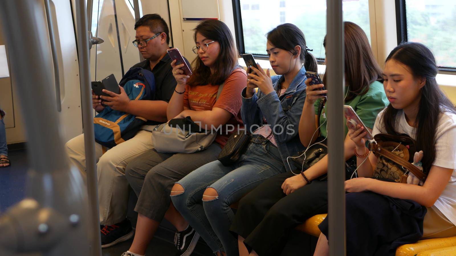 BANGKOK, THAILAND - 13 JULY, 2019: Asian passengers in train using smartphones. Thai people online surfing internet in bts car. Public transportation. Addiction from social media and phone in subway