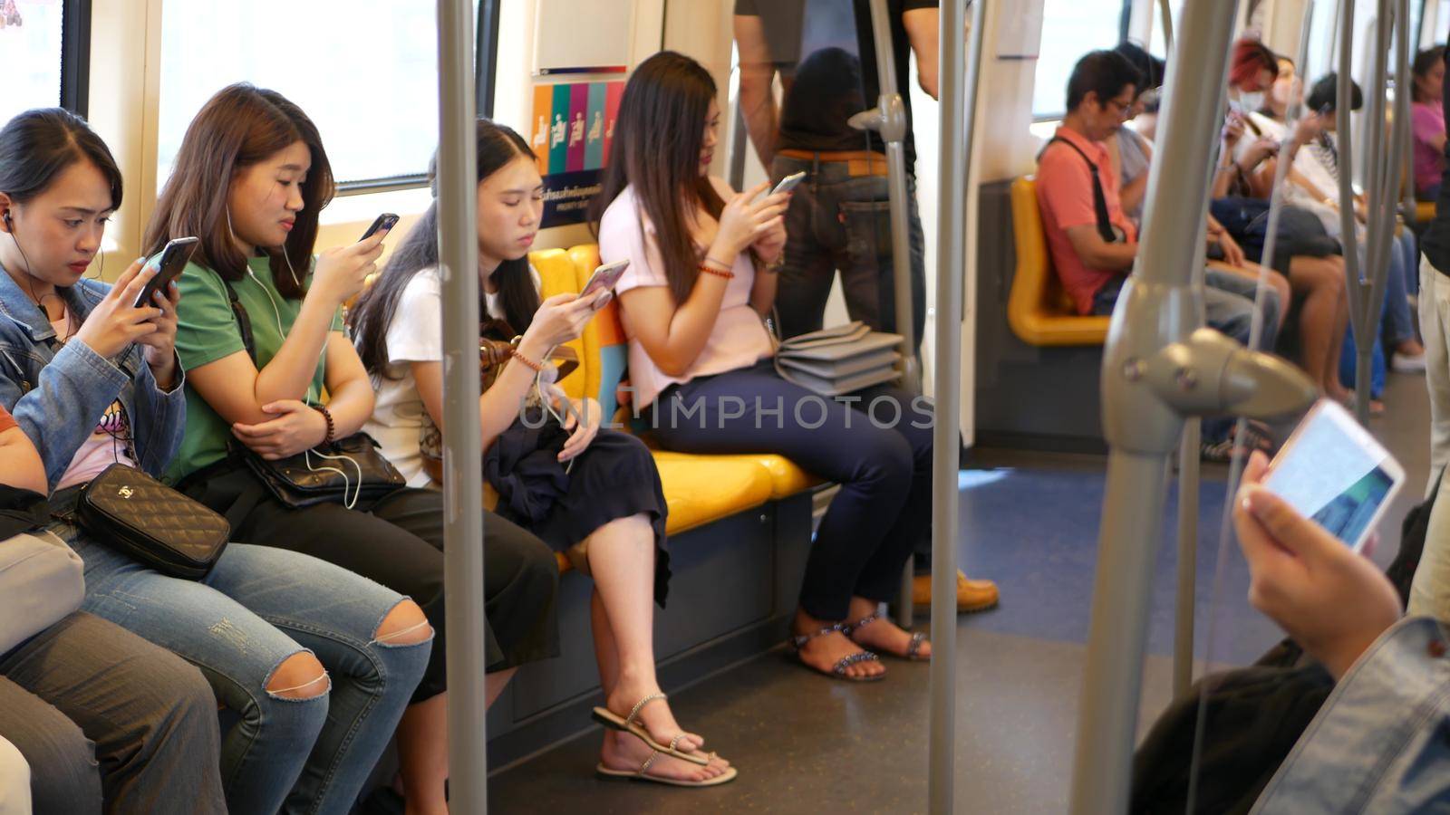 BANGKOK, THAILAND - 13 JULY, 2019: Asian passengers in train using smartphones. Thai people online surfing internet in bts car. Public transportation. Addiction from social media and phone in subway