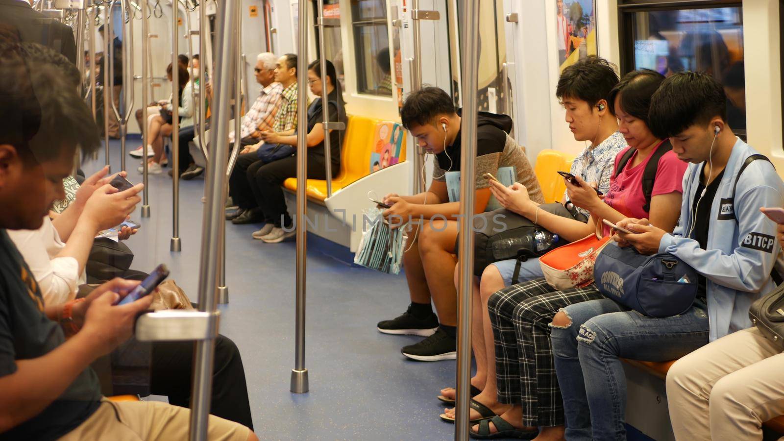 BANGKOK, THAILAND - 13 JULY, 2019: Asian passengers in train using smartphones. Thai people online surfing internet in bts car. Public transportation. Addiction from social media and phone in subway