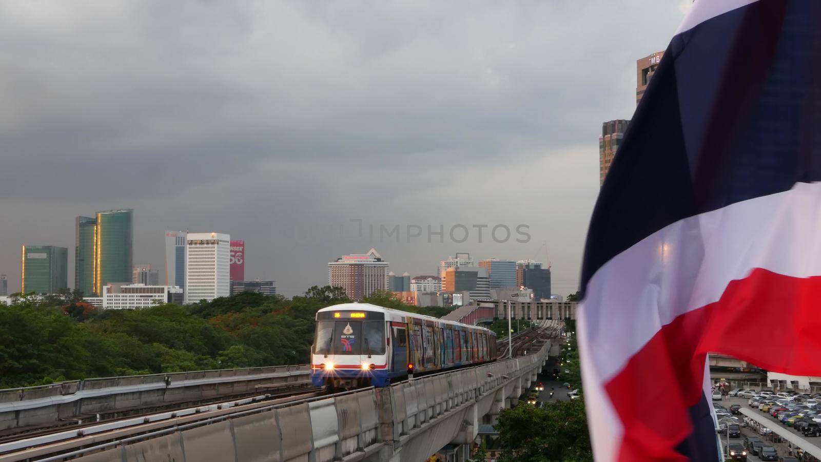 BANGKOK, THAILAND - 10 JULY, 2019: View of modern asian city from bts sky train platform. Train on metro rail road station. Public transportation in Krungtep downtown. State national flag waving