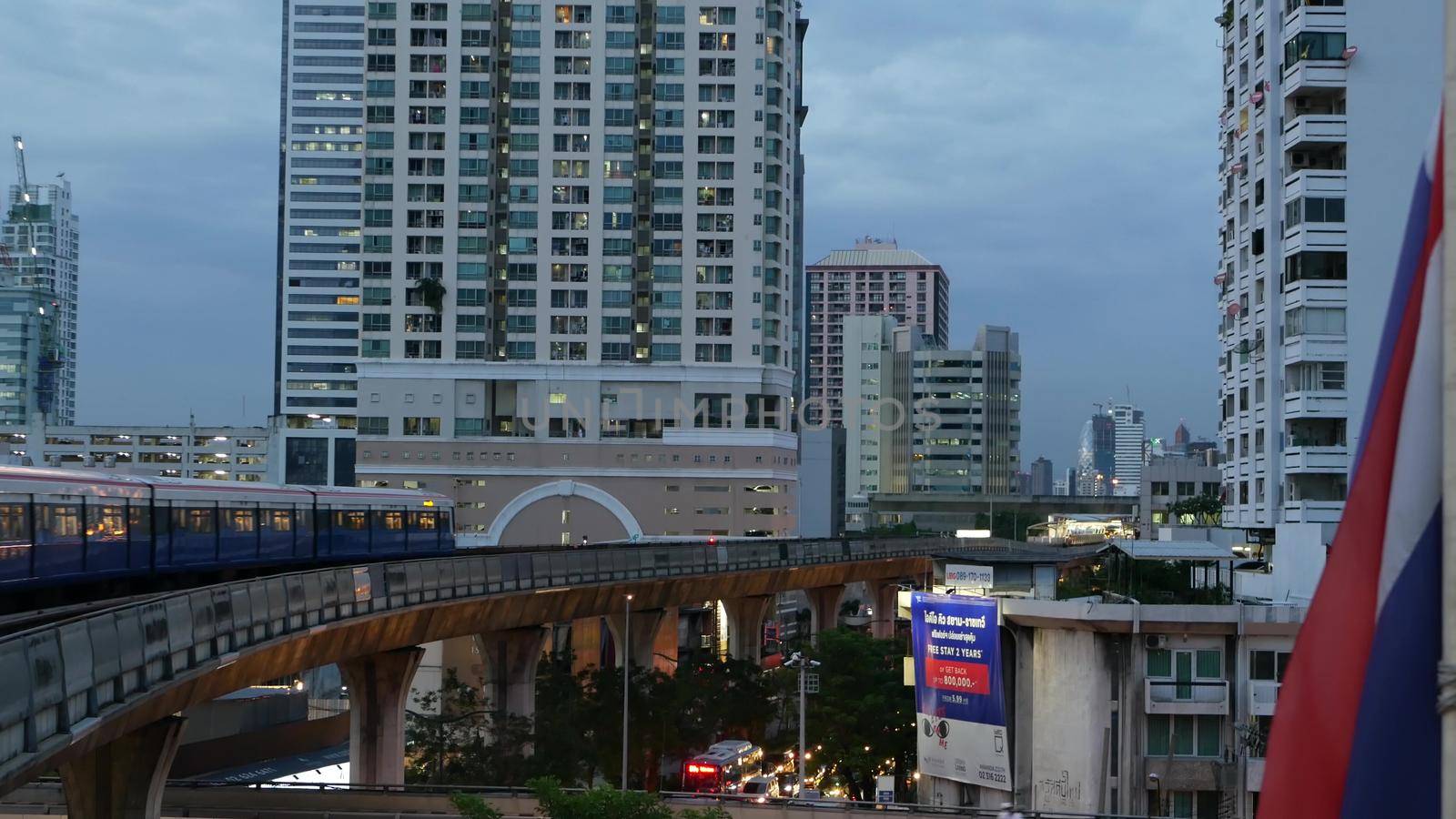 BANGKOK, THAILAND - 10 JULY, 2019: View of modern asian city from bts sky train platform. Train on metro rail road station. Public transportation in Krungtep downtown. State national flag waving