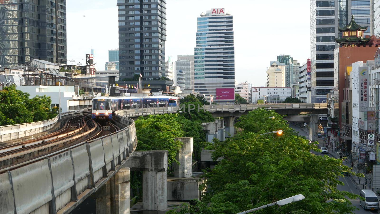 BANGKOK, THAILAND - 13 JULY, 2019: View of modern asian city from bts sky train platform. Train on metro rail road station. Public transportation in Krungtep downtown. Evening steet traffic in Asia