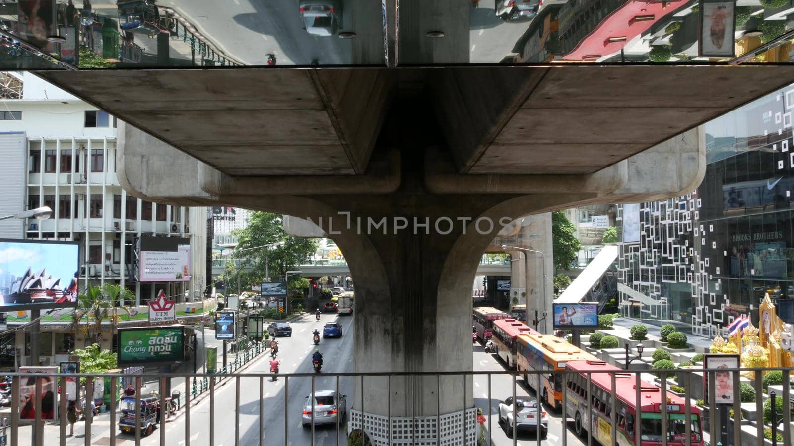 BANGKOK, THAILAND - 11 JULY, 2019 Intersection on busy city street. People on motorcycles and cars riding, pedestrian bridge. Vehicles reflected upside down in mirror. City life perspective reflection