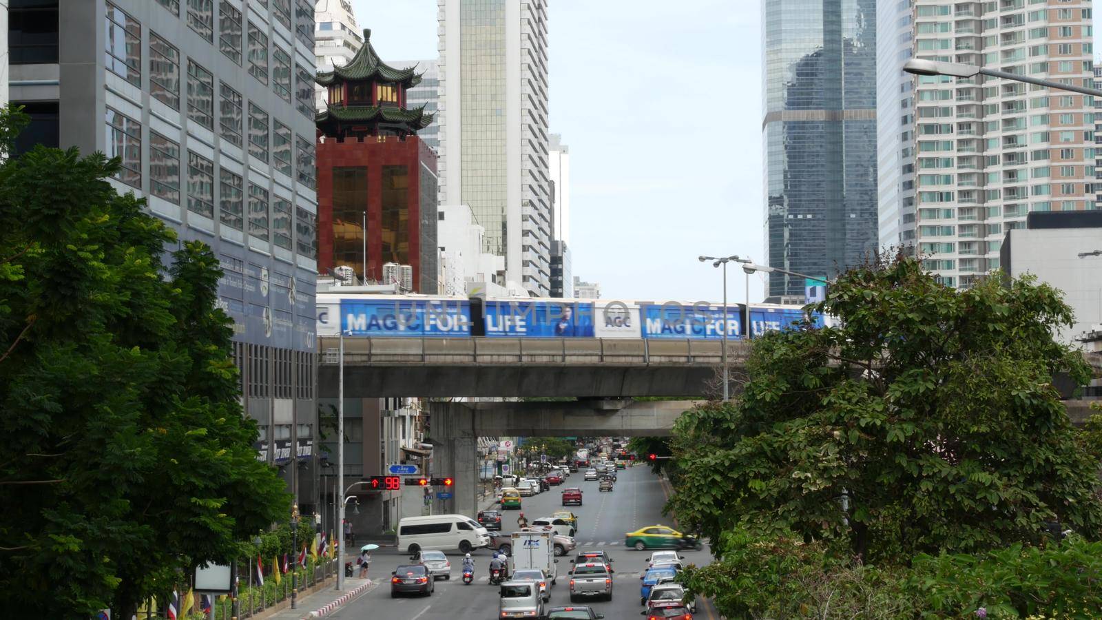 BANGKOK, THAILAND - 13 JULY, 2019: Traffic on modern city street. Contemporary train riding on railroad bridge over road with cars in center of capital