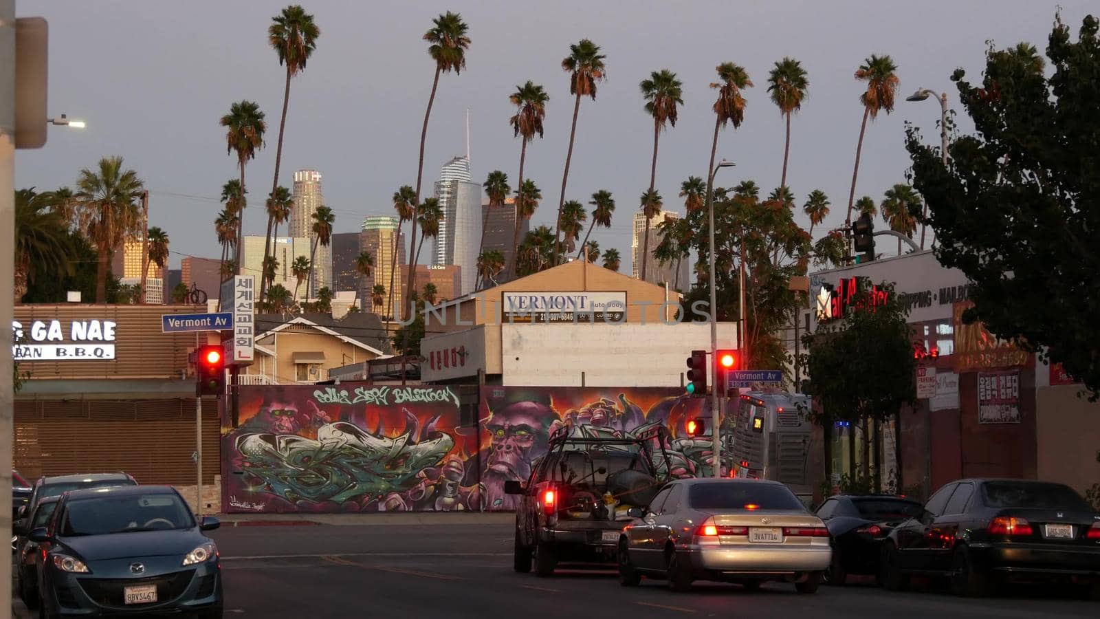 LOS ANGELES, CALIFORNIA, USA - 30 OCT 2019: Urban skyline and palms. LA city night aesthetic, graffiti painting on Vermont street. Highrise skyscrapers in downtown of metropolis. Road intersection by DogoraSun
