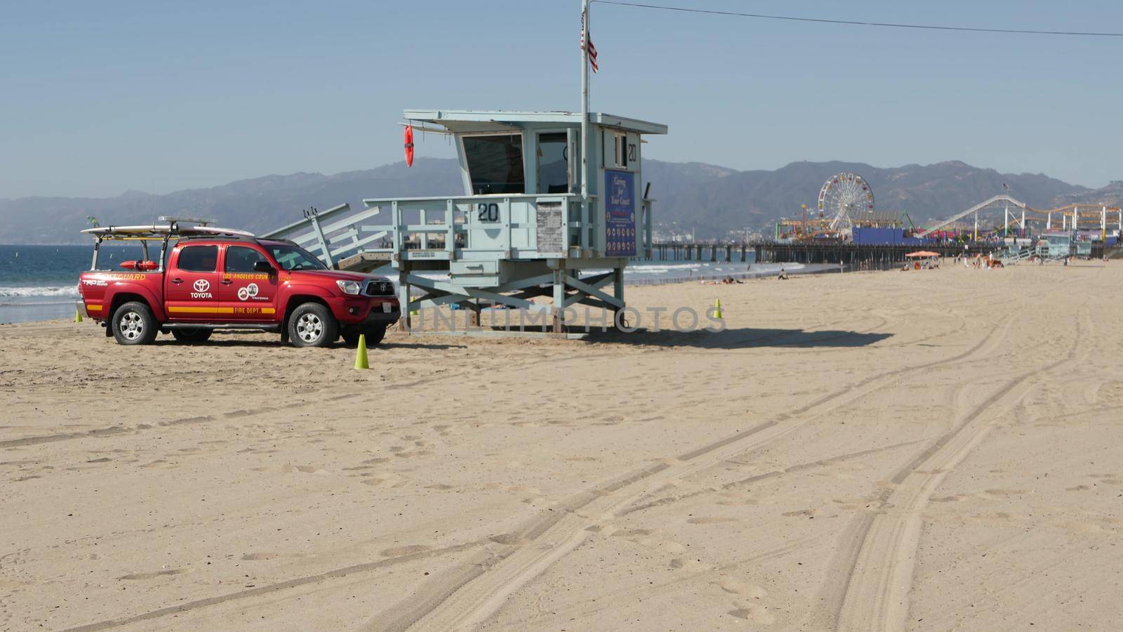 SANTA MONICA, LOS ANGELES CA USA - 28 OCT 2019: California summertime beach aesthetic. Iconic blue wooden watchtower, red lifeguard car on sandy sunny coast. Amusement park and attractions on pier. by DogoraSun