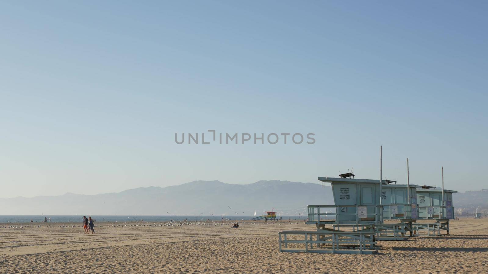 LOS ANGELES CA USA - 16 NOV 2019: California summertime Venice beach aesthetic. Sea gulls on sunny california coast, iconic retro wooden rainbow lgbt pride lifeguard watchtower near Santa Monica by DogoraSun
