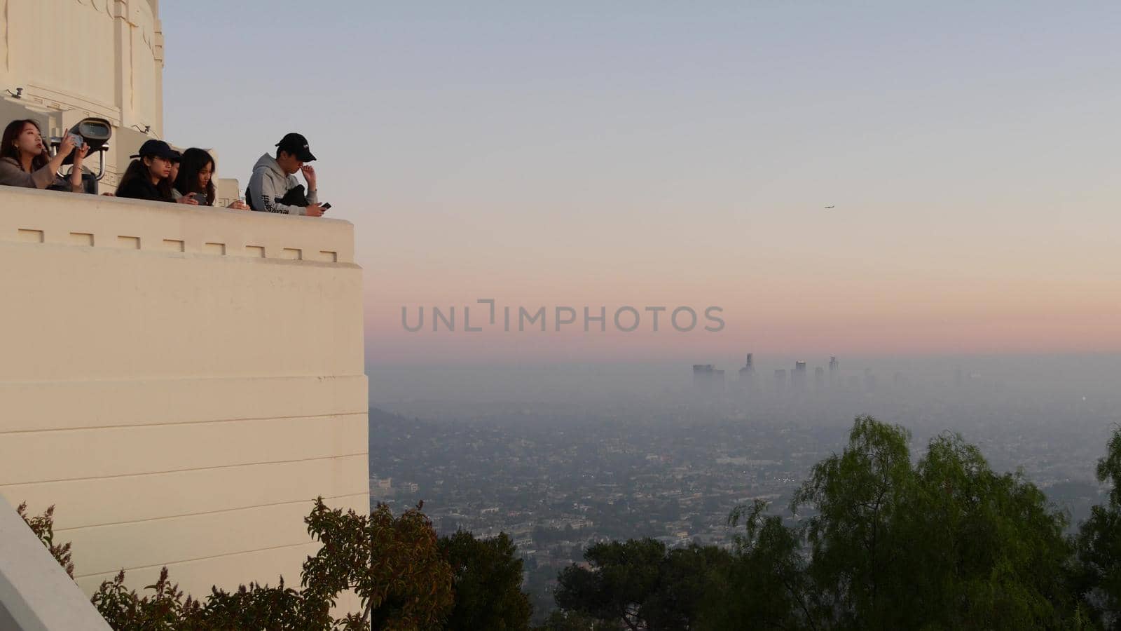 LOS ANGELES, CALIFORNIA, USA - 7 NOV 2019: Griffith observatory viewpoint. Crowd on vista point, people watching sunset over city and Hollywood sign. Many multiracial tourists look at golden sundown by DogoraSun