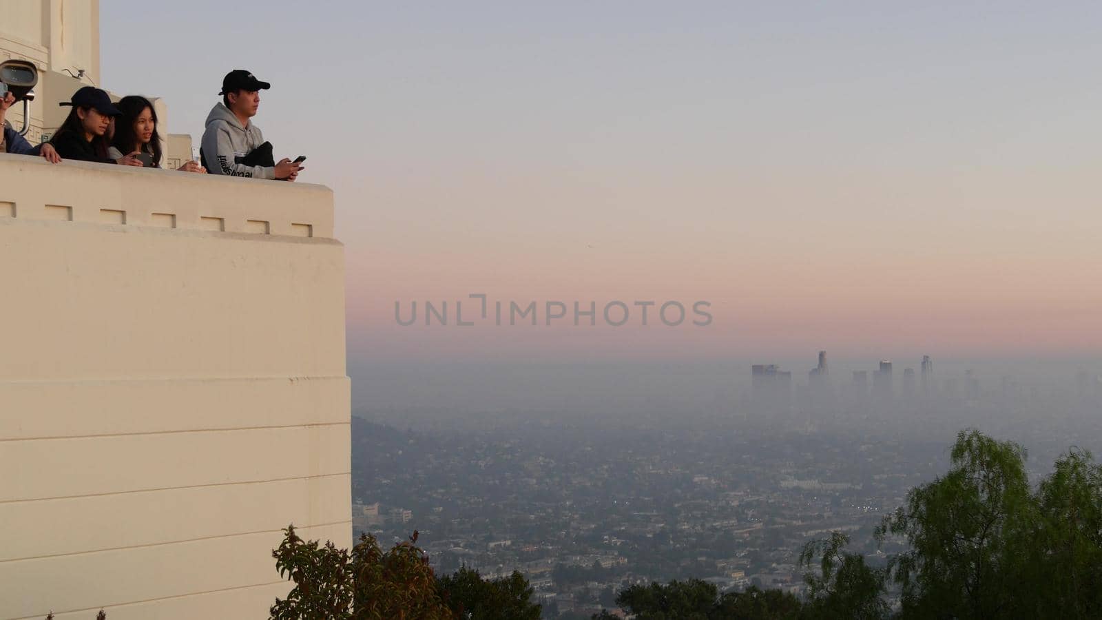 LOS ANGELES, CALIFORNIA, USA - 7 NOV 2019: Griffith observatory viewpoint. Crowd on vista point, people watching sunset over city and Hollywood sign. Many multiracial tourists look at golden sundown by DogoraSun