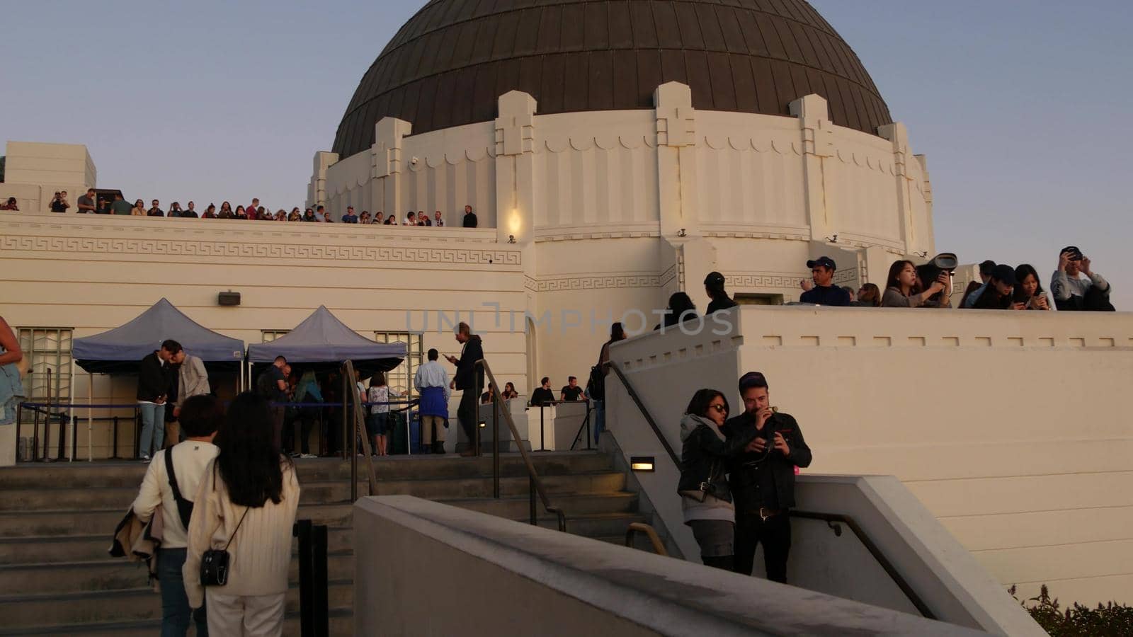 LOS ANGELES, CALIFORNIA, USA - 7 NOV 2019: Griffith observatory viewpoint. Crowd on vista point, people watching sunset over city and Hollywood sign. Many multiracial tourists look at golden sundown by DogoraSun