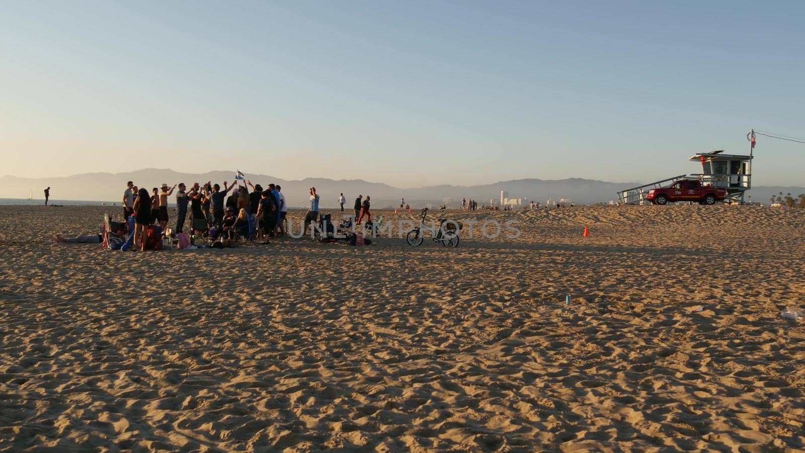 LOS ANGELES CA USA - 16 NOV 2019: California, happy young multiracial friends having fun and hanging out. Group of multiethnic people dancing on party in sunset light. Venice beach summertime leisure.