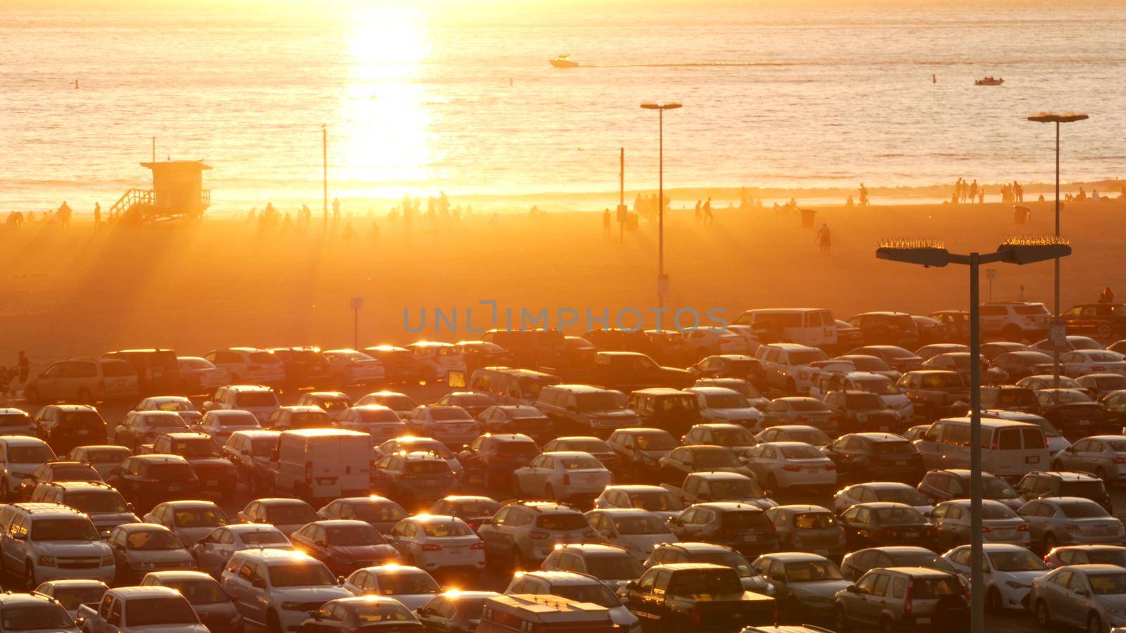 SANTA MONICA, LOS ANGELES, USA - 28 OCT 2019: California summertime beach aesthetic, atmospheric golden sunset. Unrecognizable people silhouettes, sun rays over pacific ocean waves. Lifeguard tower.