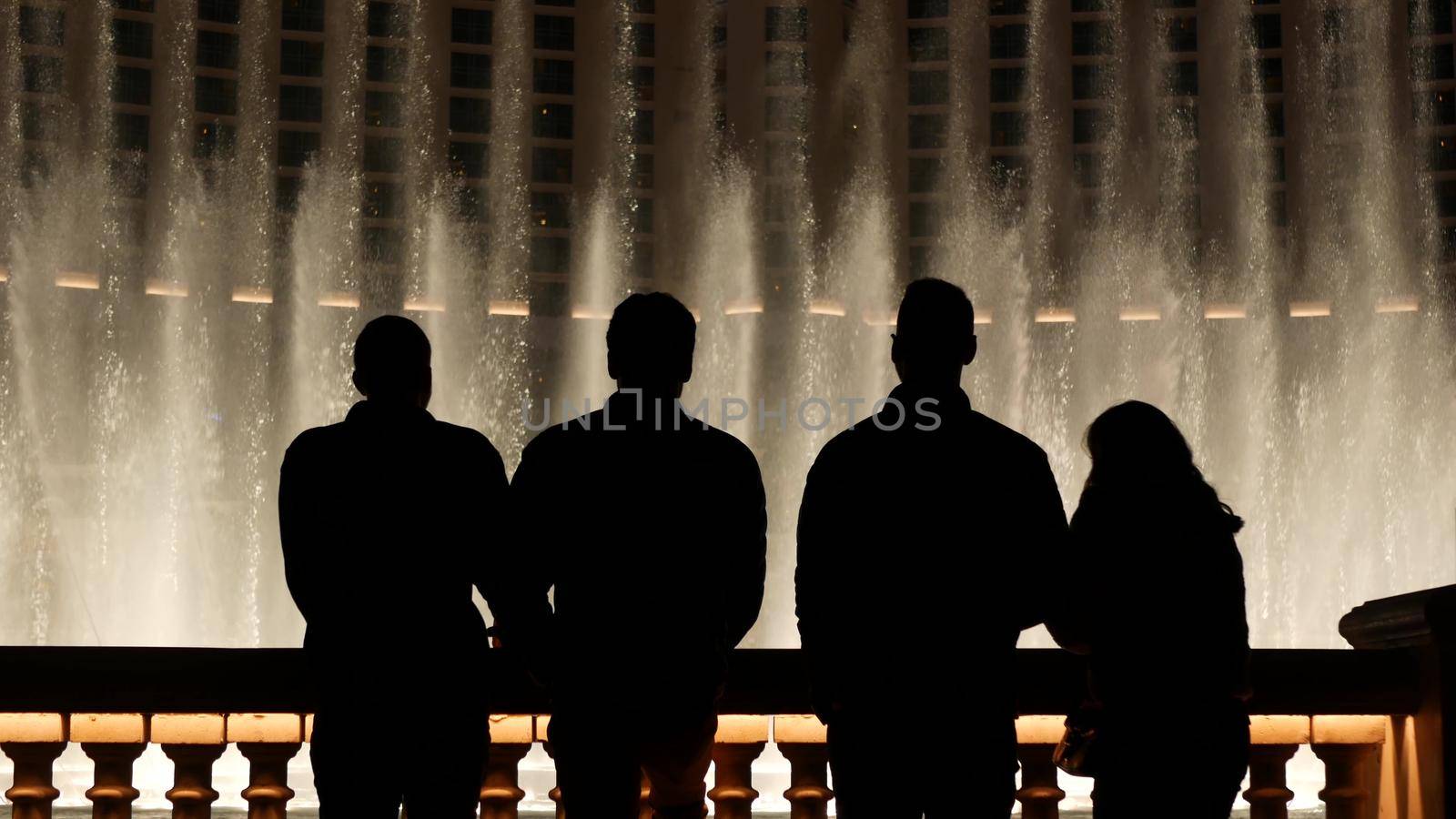 LAS VEGAS, NEVADA USA - 13 DEC 2019: People looking at Bellagio fountain musical performance at night. Contrast silhouettes and glowing dancing splashing water. Entertainment show in gambling city by DogoraSun