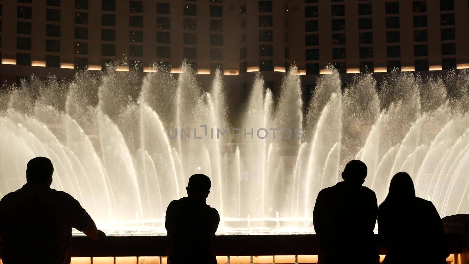 LAS VEGAS, NEVADA USA - 13 DEC 2019: People looking at Bellagio fountain musical performance at night. Contrast silhouettes and glowing dancing splashing water. Entertainment show in gambling city by DogoraSun