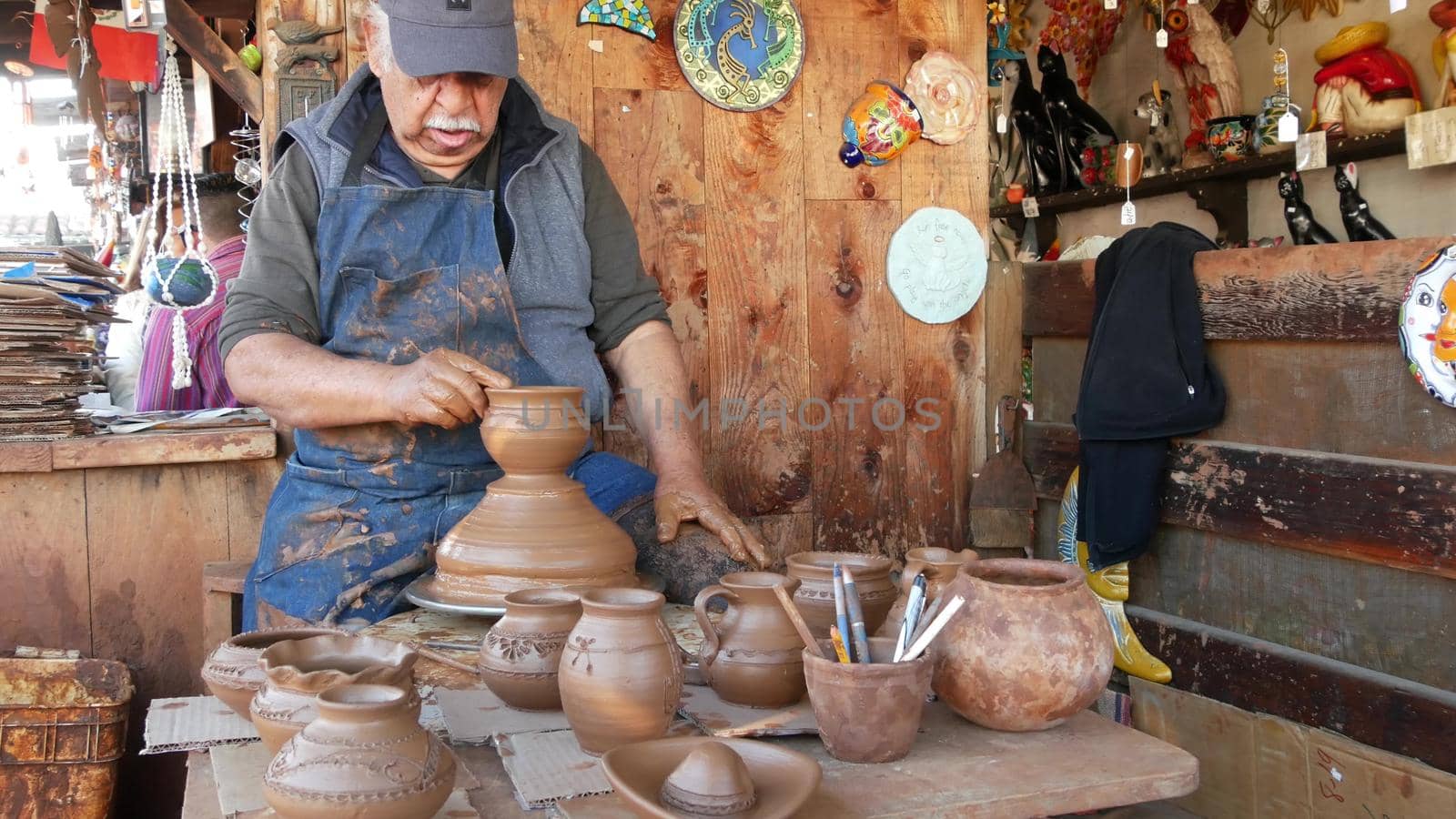 SAN DIEGO, CALIFORNIA USA - 5 JAN 2020: Potter working in mexican Oldtown, raw clay on pottery wheel. Man's hands, ceramist in process of modeling handcrafted clayware. Craftsman creating ceramic by DogoraSun