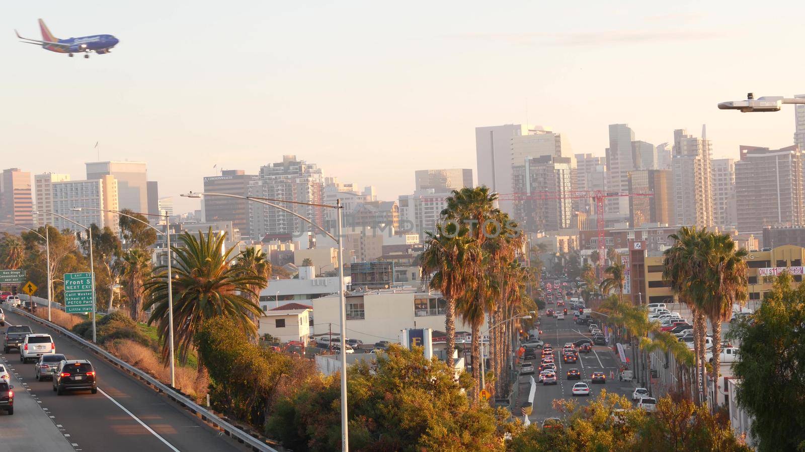 SAN DIEGO, CALIFORNIA USA - 15 JAN 2020: Busy intercity freeway, traffic jam on highway during rush hour. Urban skyline, highrise skyscraper and landing plane. Flying airplane, transportation concept by DogoraSun