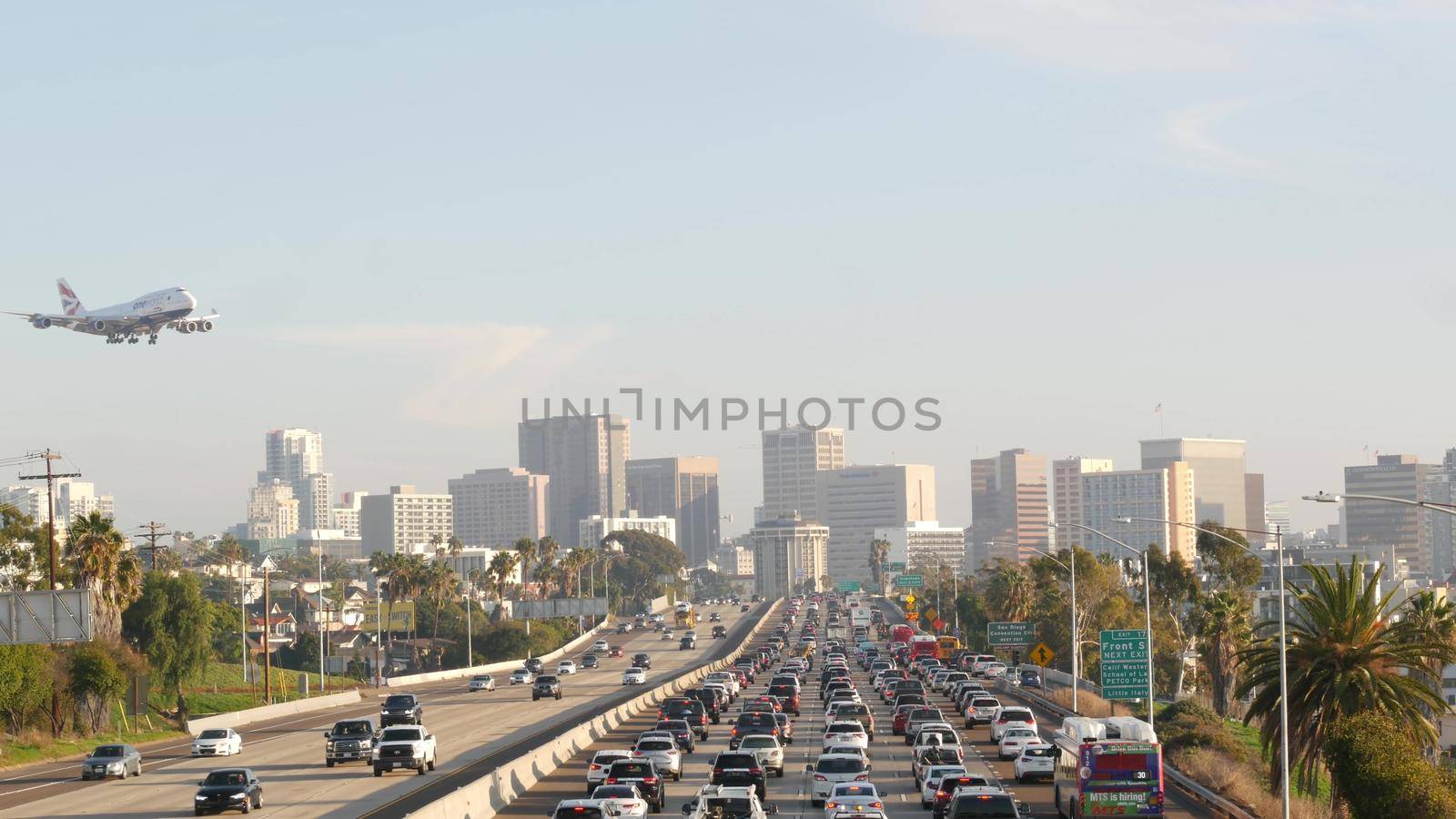 SAN DIEGO, CALIFORNIA USA - 15 JAN 2020: Busy intercity freeway, traffic jam on highway during rush hour. Urban skyline, highrise skyscraper and landing plane. Flying airplane, transportation concept.