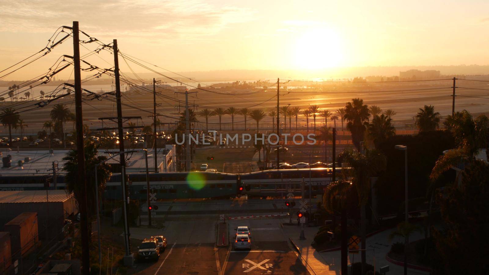 SAN DIEGO, CALIFORNIA USA - 15 JAN 2020: Level crossing near Lindbergh field international airport. Coaster railroad train and runway at sunset. NCTD rail transportation, cars and railway transport.