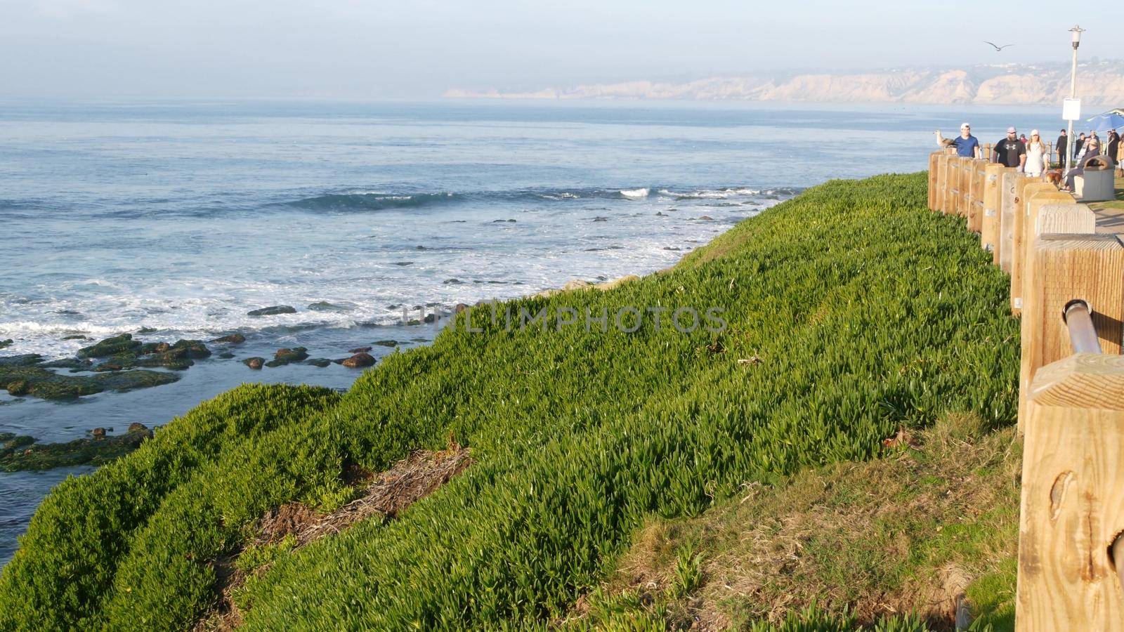 La Jolla, San Diego, CA USA -24 JAN 2020: Group of people walking on steep high cliff promenade, multiethnic pedestrians, tourists during holidays. Succulents and ocean, golden sunset in California.