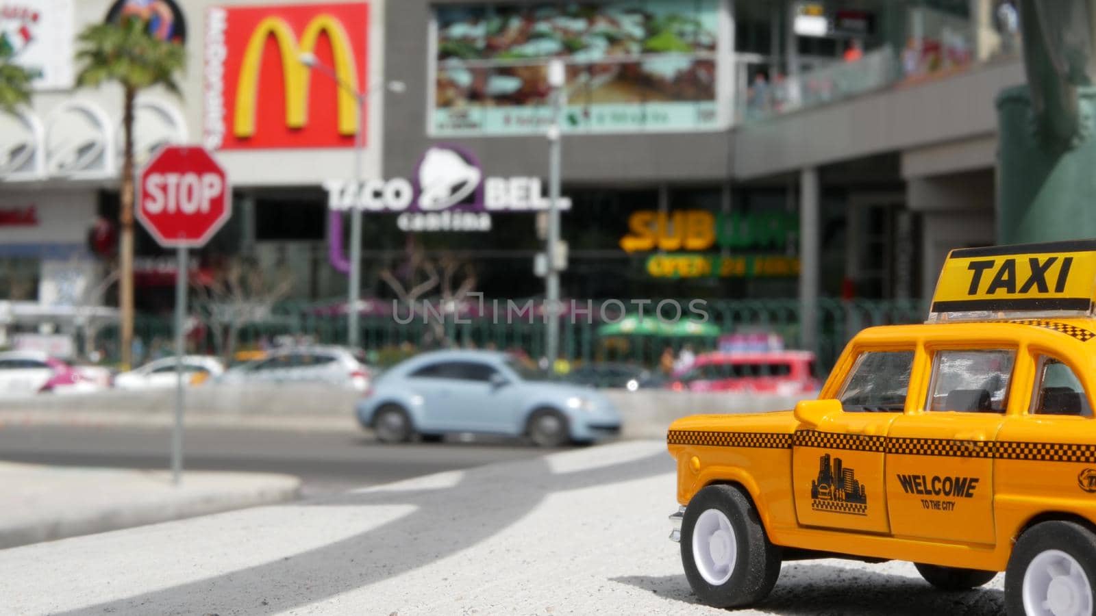 LAS VEGAS, NEVADA USA - 7 MAR 2020: Yellow vacant mini taxi cab close up on Harmon avenue corner. Small retro car model. Little iconic auto toy as symbol of transport against american shopping mall.