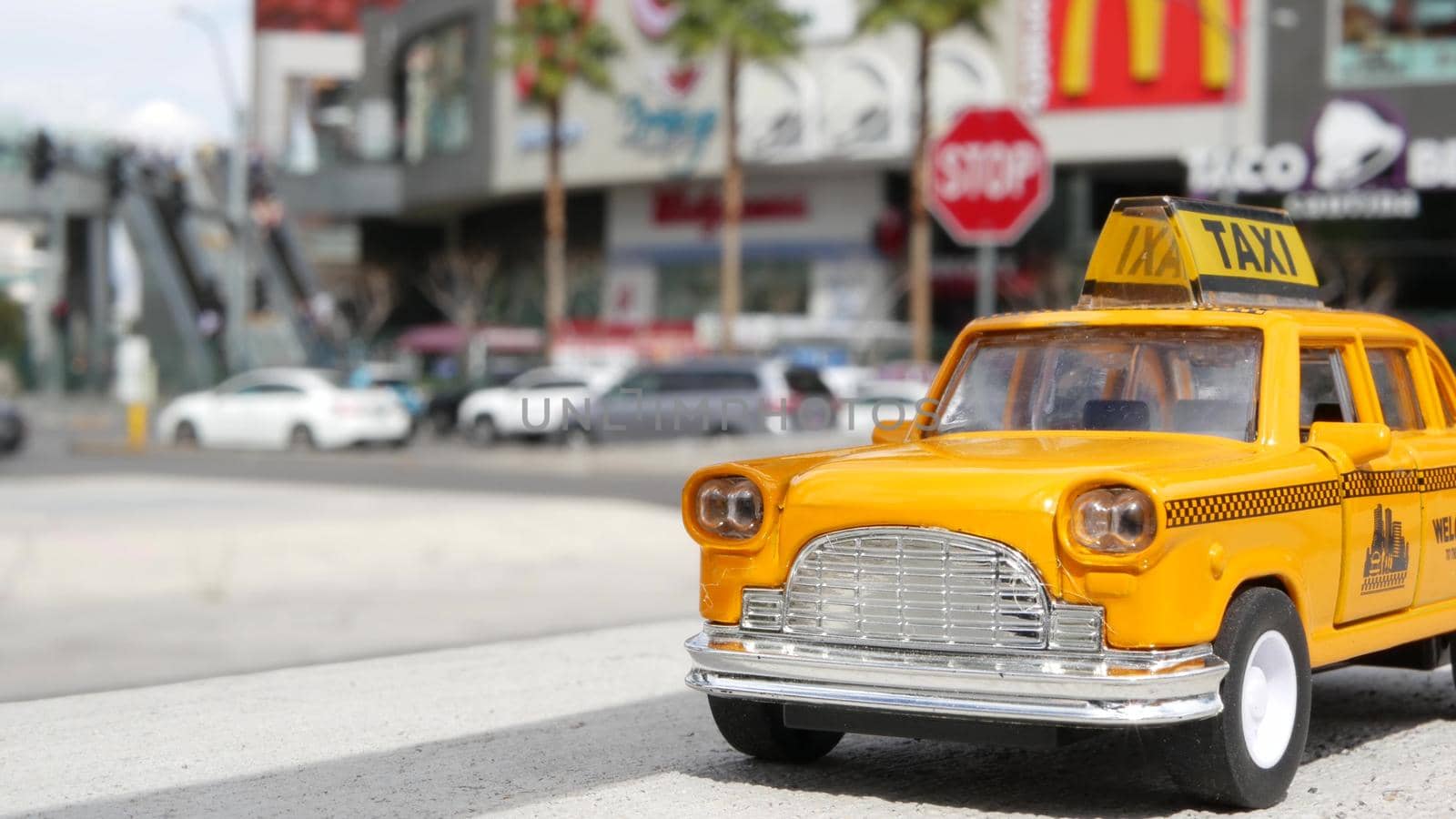 LAS VEGAS, NEVADA USA - 7 MAR 2020: Yellow vacant mini taxi cab close up on Harmon avenue corner. Small retro car model. Little iconic auto toy as symbol of transport against american shopping mall.