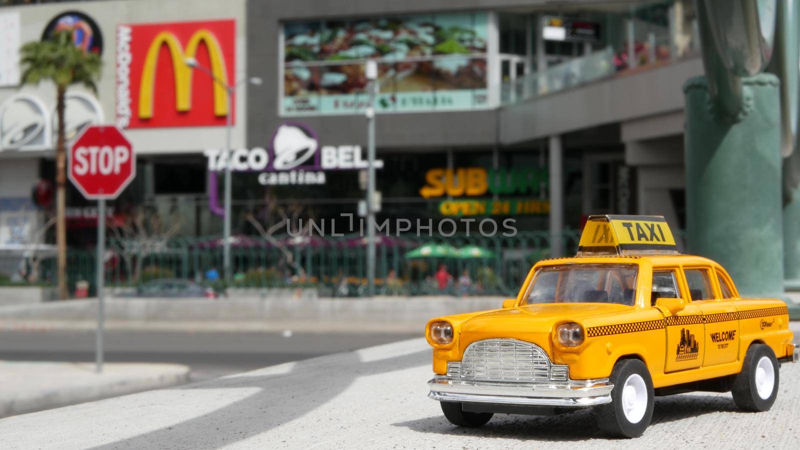 LAS VEGAS, NEVADA USA - 7 MAR 2020: Yellow vacant mini taxi cab close up on Harmon avenue corner. Small retro car model. Little iconic auto toy as symbol of transport against american shopping mall by DogoraSun