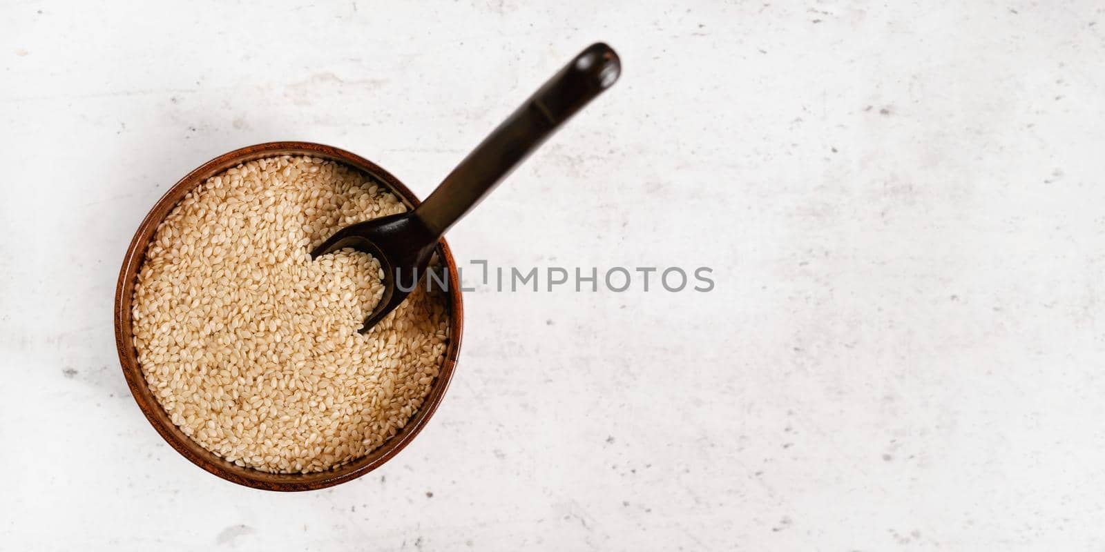 White sesame - Sesamum indicum - seeds in small wooden cup on white stone like board, view from above, space for text right side.