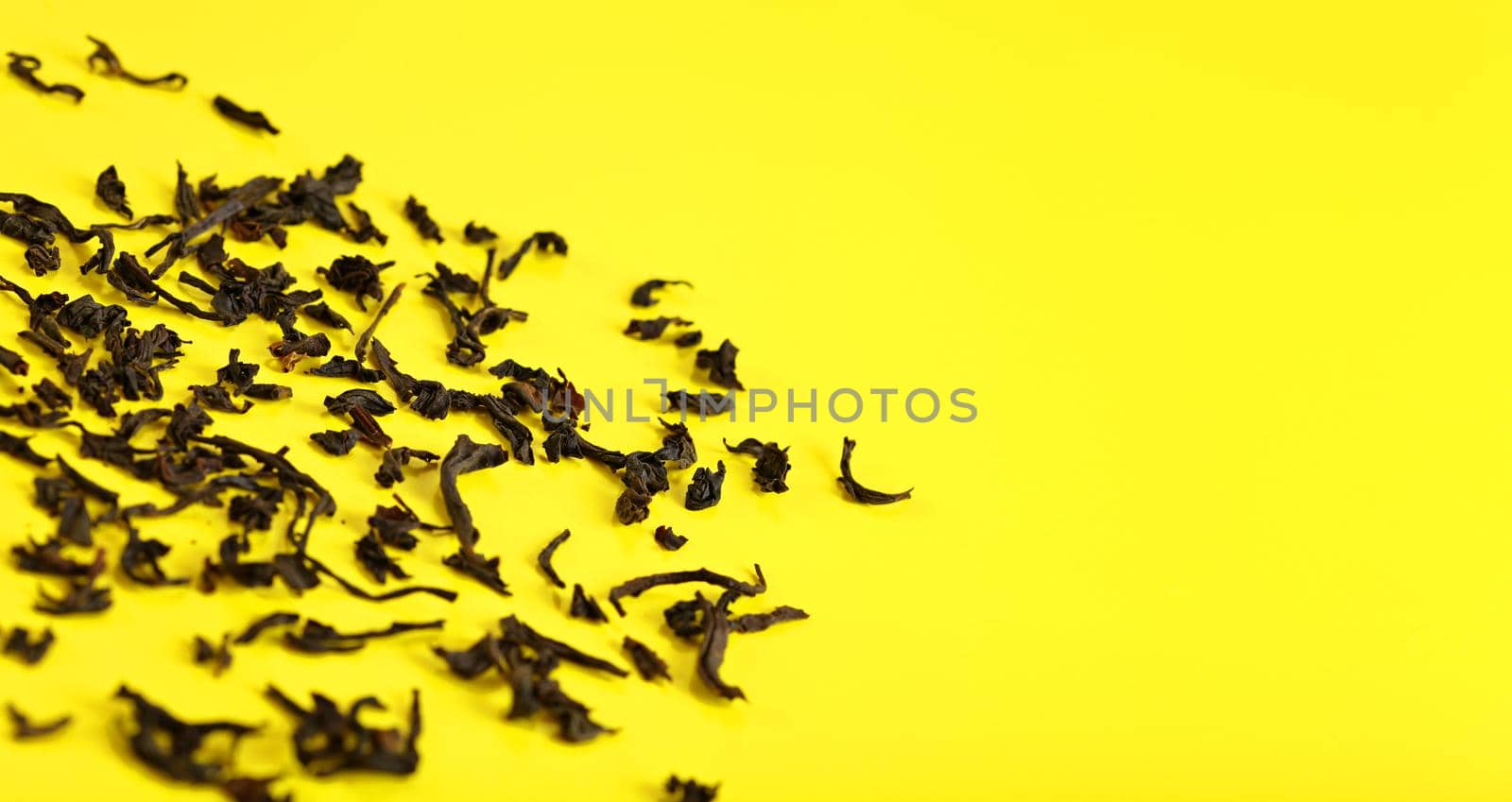 Dry black loose tea leaves on yellow board, closeup detail from above, space for text right side by Ivanko