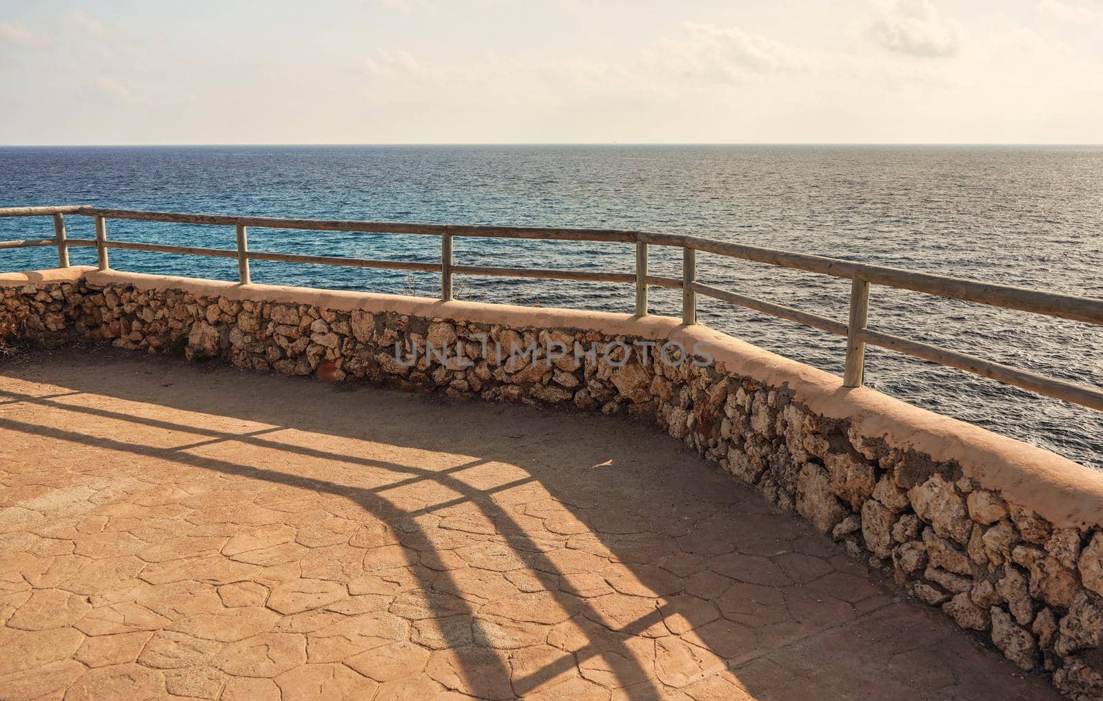 Stone road with wooden fence by sea cliff lit by morning sun.