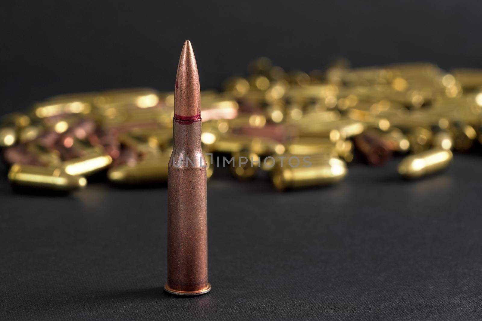 Copper machine gun bullet, more blurred yellow ammo on black board background.