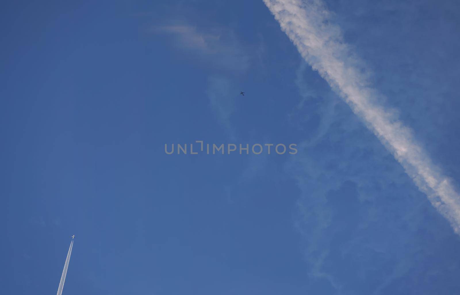 White trails from commercial airplanes, another plane flying, chemtrails conspiracy theory concept.