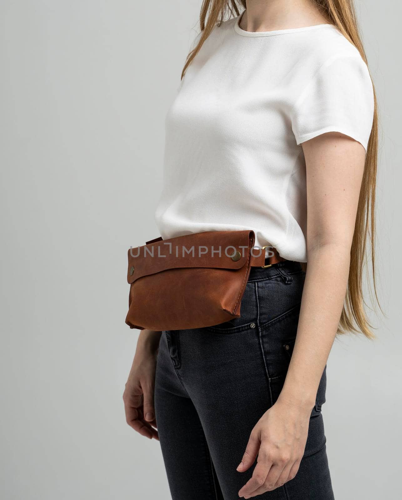Girl in a white blouse with a leather red handmade bag over her waist. Designer dark brown banana bag. Woman in a studio. Comfortable small bag for walking