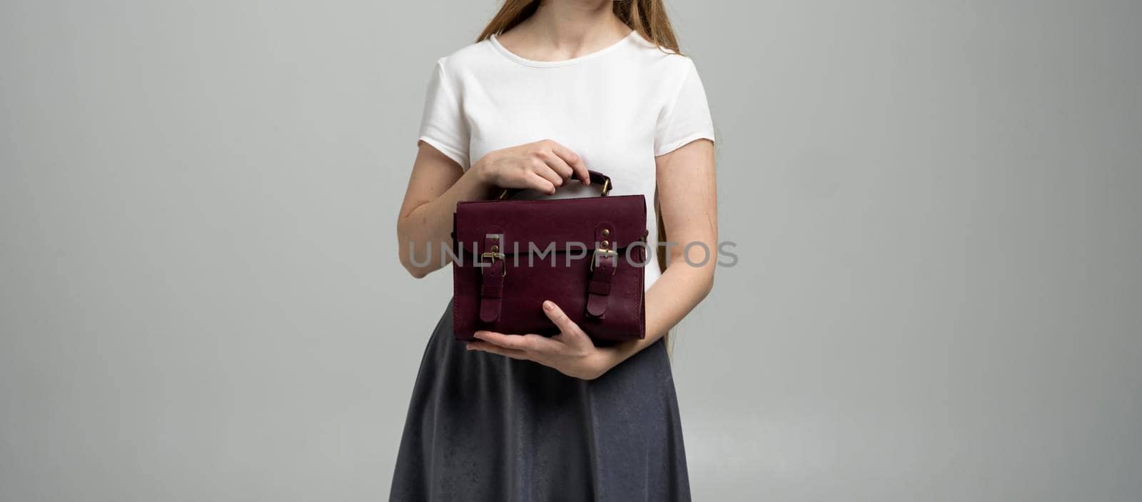 Small red leather bag in a woman's hand on a white background. Shoulder handbag. Woman in a white shirt and grey skirt and with a red handbag. Style, retro, fashion, vintage and elegance