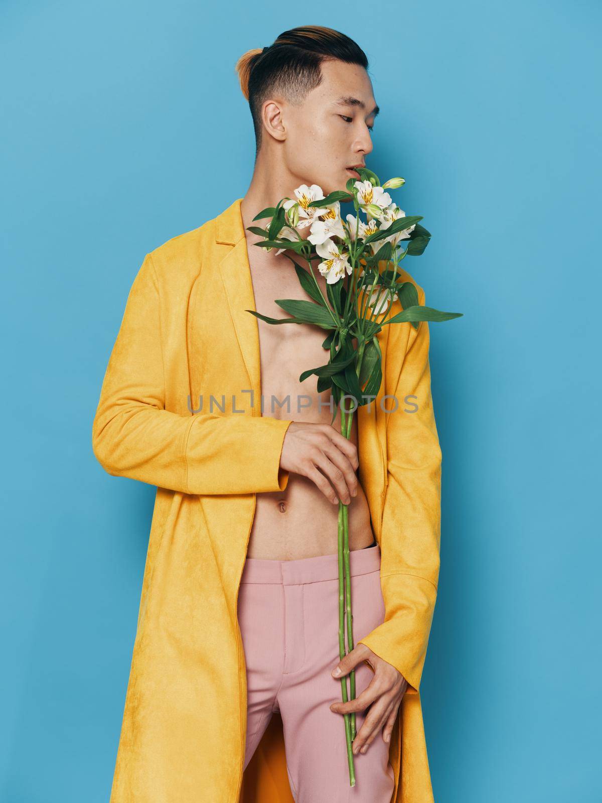 sexy asian man with bouquet of flowers looking to the side on blue background. High quality photo