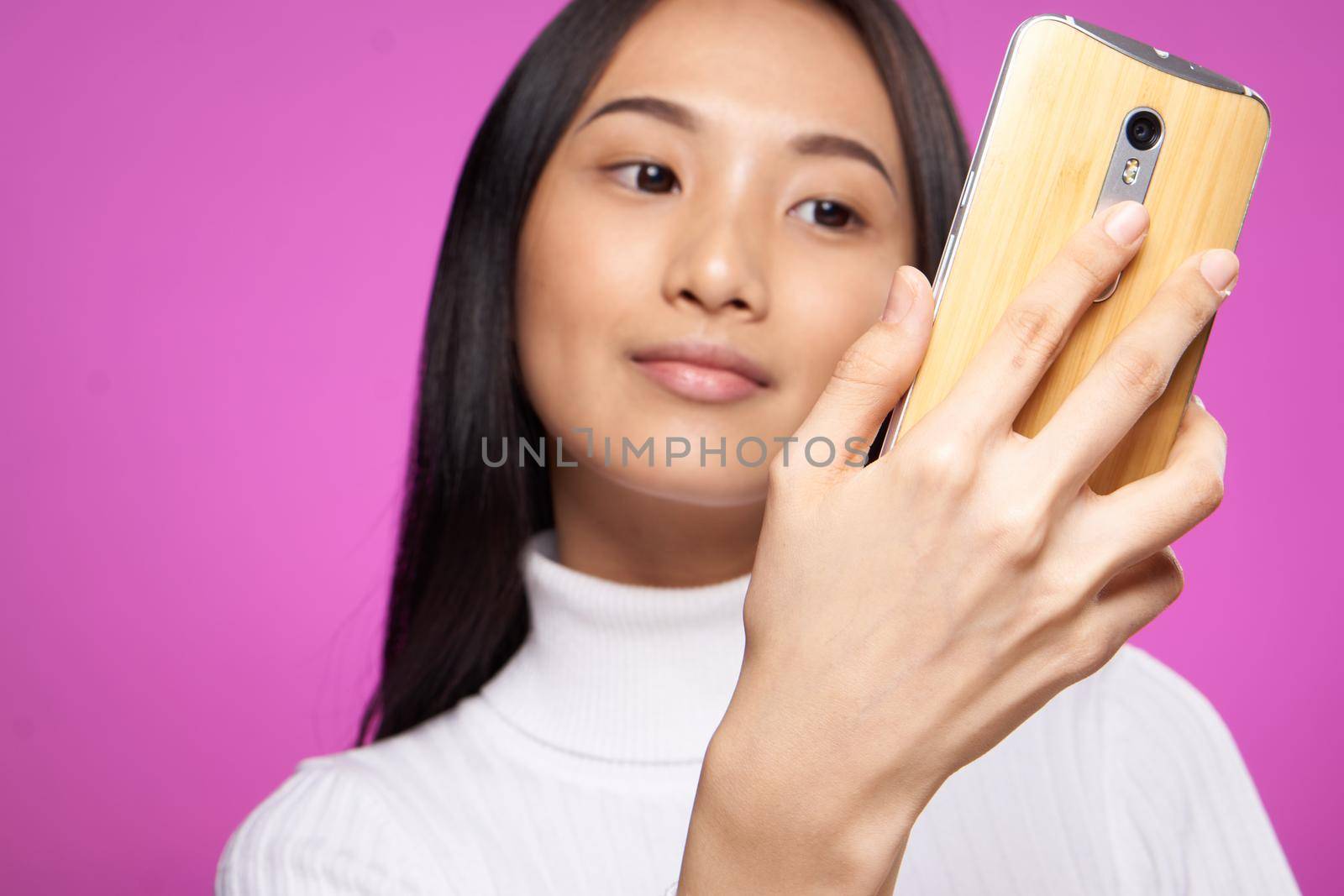 pretty asian woman with a phone in her hands looking at the screen close-up pink background by SHOTPRIME