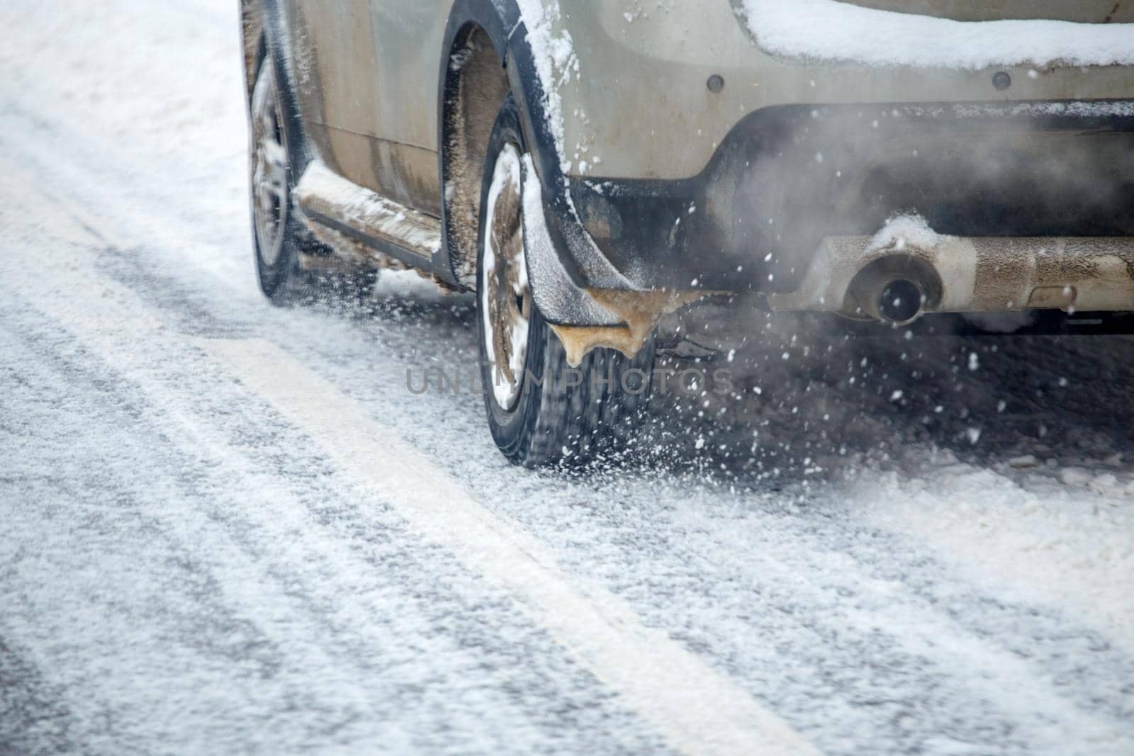 Road snow pieces flow from wheels of dirty gray car moving fast in daylight city with selective focus. by z1b